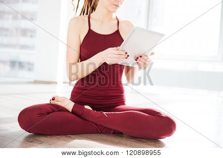 Pretty young woman dancer sitting with legs crossed and using tablet