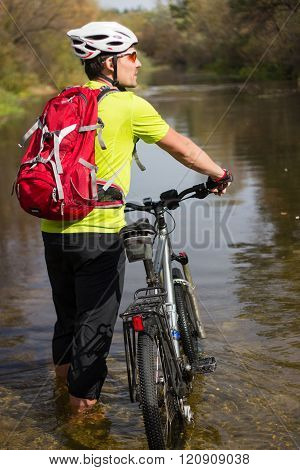 A man passes a river with a bicycle on his shoulder in a helmet and a backpack.