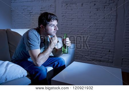 young television addict man sitting on home sofa watching TV and drinking beer bottle looking mesmerized enjoying movie sitcom or live sport at night