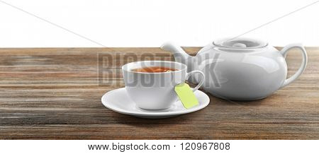 Cup of tea with tea bags and teapot on wooden background against grey background