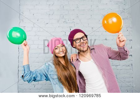 Positive Couple In Love In Caps And Glasses Holding Balloons
