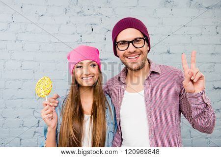 Cheerful Happy Couple Holding Lollipop And Gesturing With Two Fingers