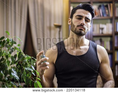 Handsome muscular young man in his home spraying cologne or perfume on neck