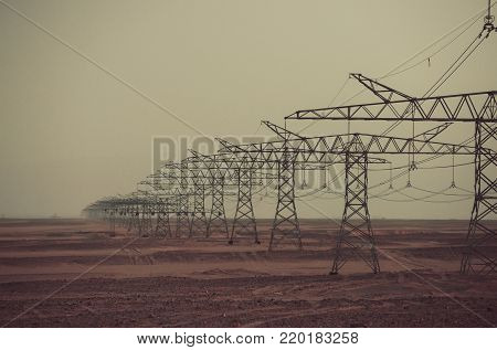 Power line towers in desert on grey sky background. Global warming, climate change. Electric energy transmission. Ecology, eco power, technology concept. Electricity distribution stations.