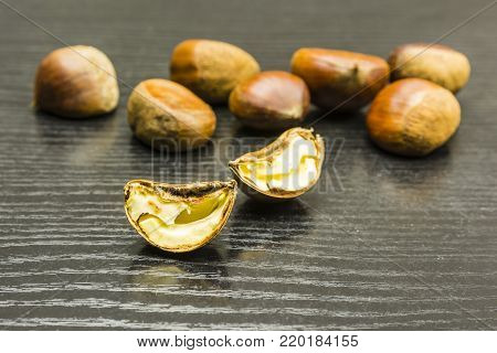 A cut ripe chestnut on a wooden dark table. In the background, whole chestnuts.
