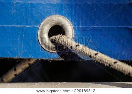 old rusty eyelets on an aged blue coated plastic canvas for agricultural and temporally use hanging in a