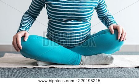 Pregnant woman practicing yoga exercise at home. Pregnancy yoga and indoors fitness concept. Ungraded low contrast footage with natural window light.