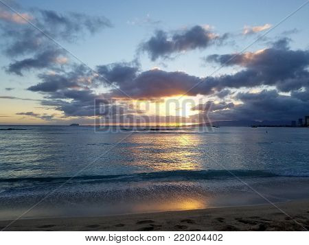 Dramatic Sunset over the clouds and reflecting on the Pacific ocean with boats on the water on Waikiki beach on Oahu, Hawaii with Waianae Mountain range visible.