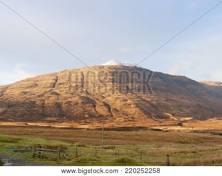 View over  autumnal orange bare landscape, sinle road,  meanders, high  rocky hills and past pastures.