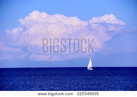 Far A lonely white yacht in the blue sea before a storm, a stormy cloud and a bright sky