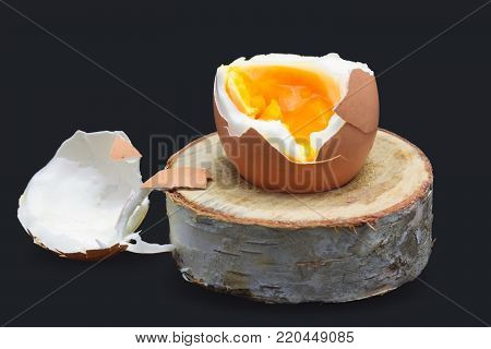 Boiled fresh egg for the breakfast on the wooden birch stand for eggs isolated on dark blue. Broken beige hen egg and pieces of shells, bright orange yolk