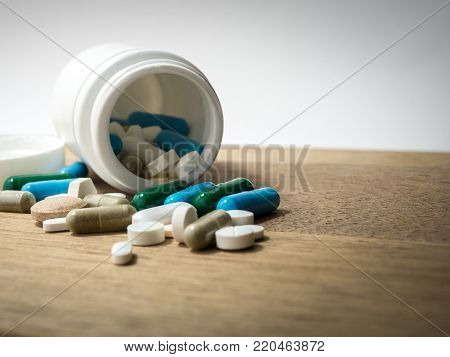 Multicolored of Drug and capsule is on the wooden table. Closeup. We are against drugs (anti drugs), cure in container for health.Heap of green blue white round capsule pills with medicine antibiotic