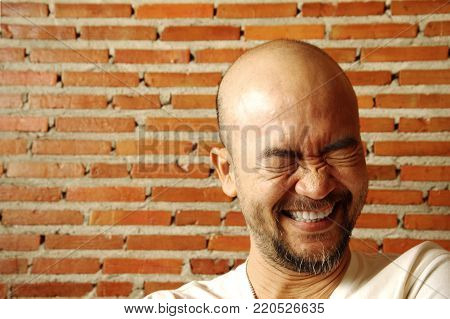 portrait cool Asian Japanese beard bald laughing man with brick wall background