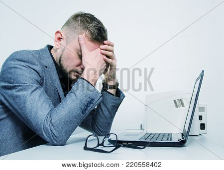a tired man with his hands on the his face at the table with a laptop in the office. toned.