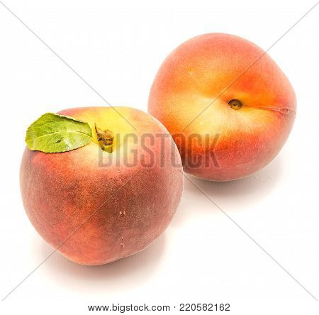 Two whole peaches, one with green leaf, isolated on white background