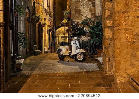 Pitigliano, Tuscany, Italy - September 30, 2016: alley at night in the old town with a vintage Italian scooter Vespa. Photo taken on September 30, 2016 in Pitigliano, Grosseto, Tuscany, Italy