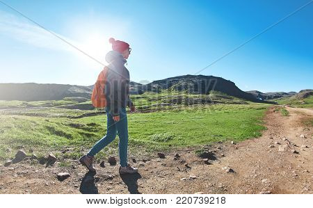 back view of woman traveler with small orange backpack on a walk in the Valley of the river of Hveragerdi Iceland. Hiking Tour of Reykjadalur Hot Springs