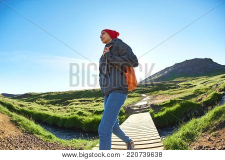 portrait of woman traveler with small orange backpack on a walk in the Valley of the river of Hveragerdi Iceland. Hiking Tour of Reykjadalur Hot Springs