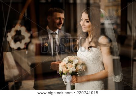 elegant brunette bride with a bouquet of roses hugs a stylish bridegroom, while he kisses her
