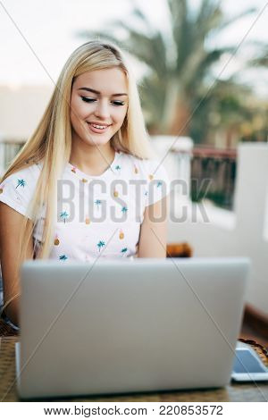 Blonde Girl Is On The Mobile Phone While Sitting In Cafe On Teracce. Young Woman Checking The Inform