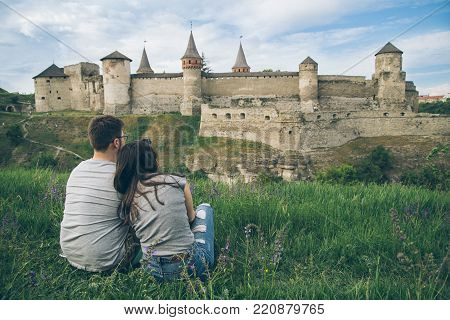 young man with woman  sit  on the grass in front old castle