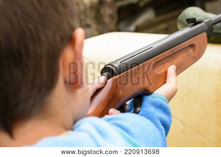 A boy shooting from an air rifle to a target. A boy with a gun in his hand. Shooting training from a gun. Dangerous game of little boy.