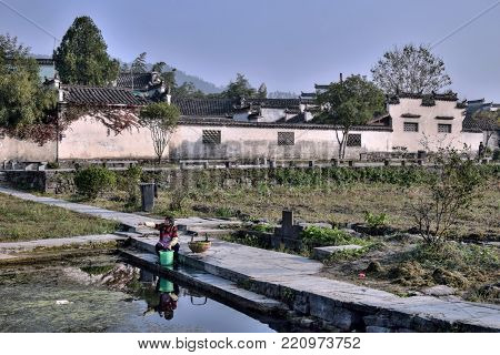 XIDI, ANHUI PROVINCE, CHINA - CIRCA OCTOBER 2017:  A woman washing the clothes in a bank of a pond in Xidi, a small ancient village in Anhui province in China near the Yellow Mountains.