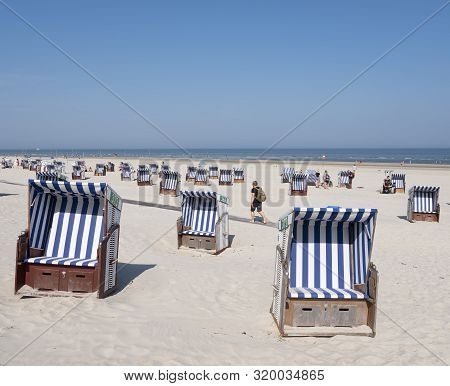 Norderney, Germany, 25 August 2019: Man With Rucksack Passes Beach Korbs On The Island Of Norderney 