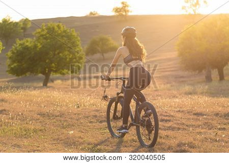 Girl On A Mountain Bike On Offroad, Beautiful Portrait Of A Cyclist At Sunset, Fitness Girl Rides A 