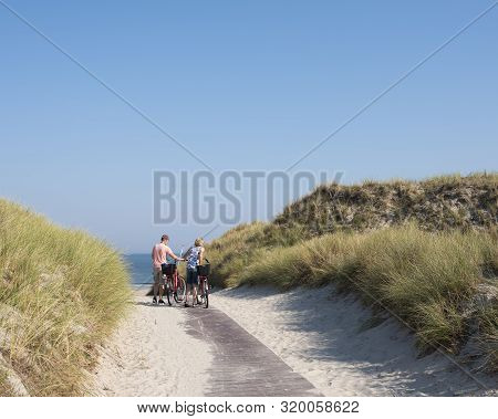 Norderney, Germany, 25 August 2019: Couple With Bicycles At Top Of Dunes Near Sea On German Island O