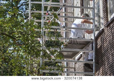 Professional Painter With Sander Sitting On A Scaffolding In Rotterdam In The Netherlands