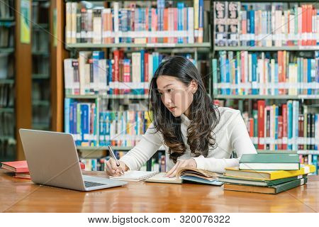 Asian Young Student In Casual Suit Doing Homework And Using Technology Laptop In Library Of Universi