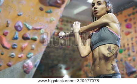 Athletic Woman With Muscular Naked Torso Doing Stretching Before Climb In Indoor Climbing Gym.