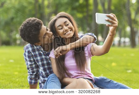 Capturing Happy Moments. Two Black Cheerful Teenagers Embracing And Making Selfie Outdoors