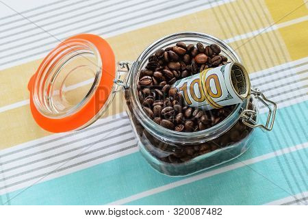Roll Of One Hundred Dollar Bills In A Clip Top Glass Jar With Coffee Beans On A Tablecloth. Can For 