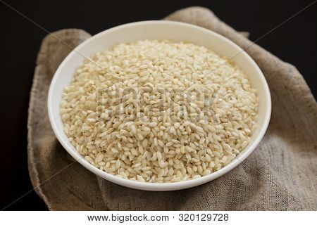 Organic Arborio Rice In A White Bowl On A Black Background, Low Angle View. Close-up.