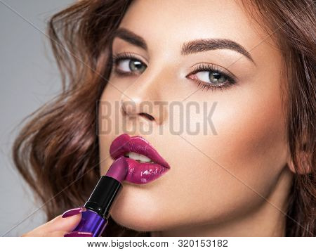 Young beautiful girl paints lips with purple  lipstick.  Young caucasian girl doing makeup. Model. Closeup woman's portrait. Vivid make-up.  Violet lips. 