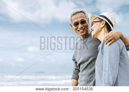Asian Senior Couple Or Elderly People Walking And Siting At The Beach On Their Weekend Vacation Holi