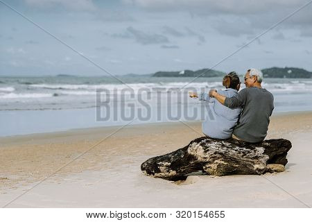 Asian Senior Couple Or Elderly People Walking And Siting At The Beach On Their Weekend Vacation Holi