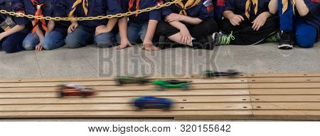 Action Shot Of Pinewood Car Race With Excited Boys In Background