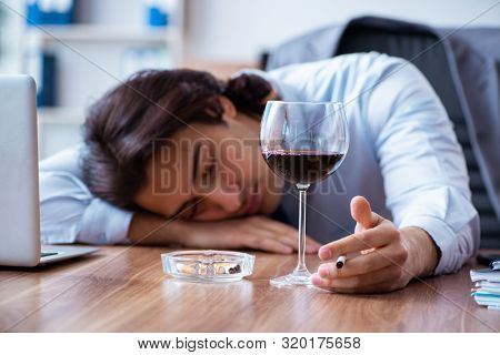Male employee drinking alcohol and smoking cigarettes at workpla