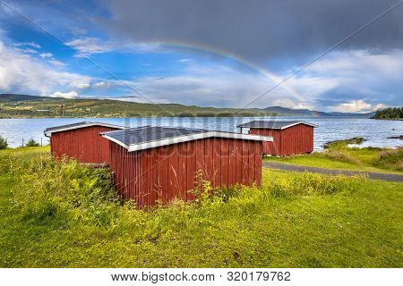 Idyllic Red Wooden Cabins Overseeing Lake Near Lillehammer, Norway. Under A Rainbow