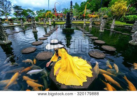 Woman Feeding Colorful Fish In Pond At Tirta Gangga Water Palace In Bali, Indonesia.