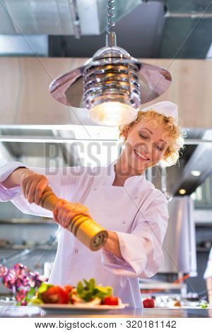 Mature chef using peppermill on salad in plate at restaurant