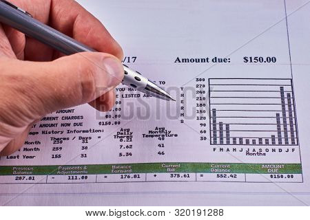 Mans Hand With Pen And Utility Bill With Annual Spending Chart. Close-up