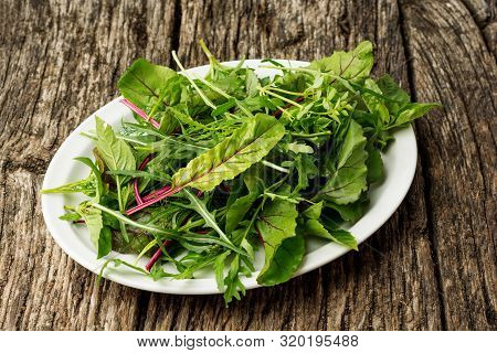 Fresh Salad Plate With Mixed Greens Arugula, Mesclun, Mache On Dark Wooden Background Close Up. Heal