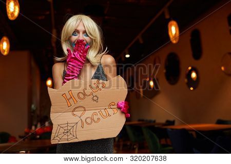 Waist Up Portrait Of Young Woman Wearing Halloween Costume Posing With Hocus Pocus Sigh During Party