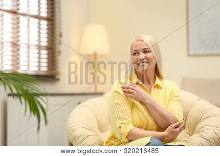 Portrait Of Happy Mature Woman Sitting In Papasan Chair At Home