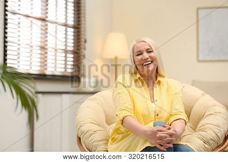 Portrait Of Happy Mature Woman Sitting In Papasan Chair At Home