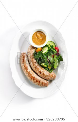 Top view of Munich sausages for frying made from pork and beef with mustard sauce and mixed salad isolated. Traditional German rostbratwurst, wurst or bratwurst with vegetables and greens topview